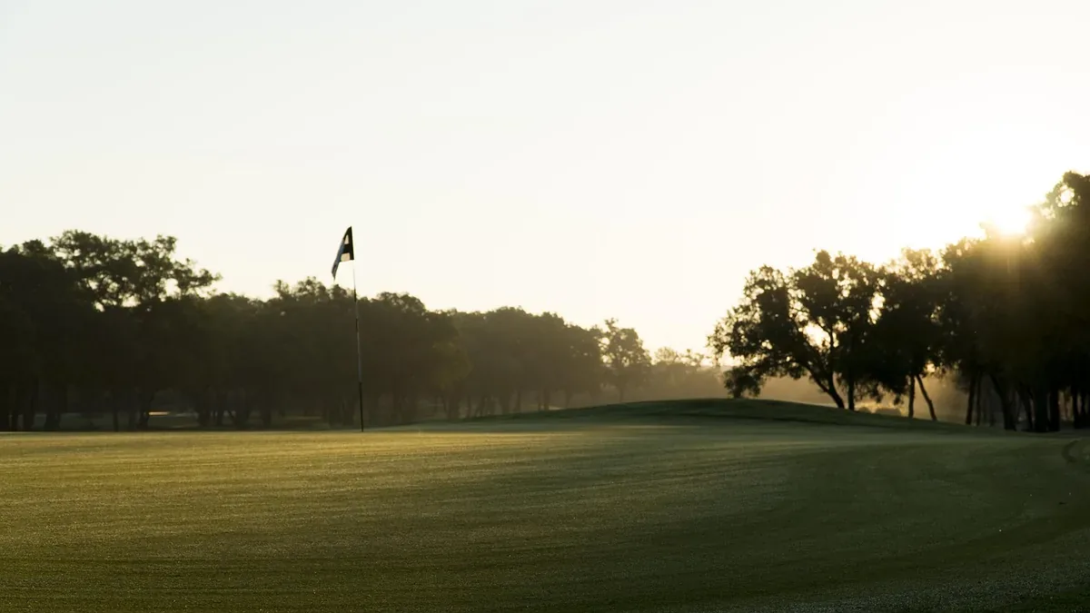 A golf flag on the green in low morning light with mist through the trees